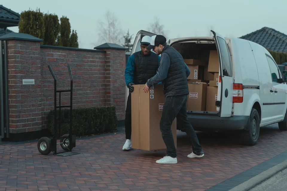 Deux manutentionnaires chargent un grand carton dans un fourgon.